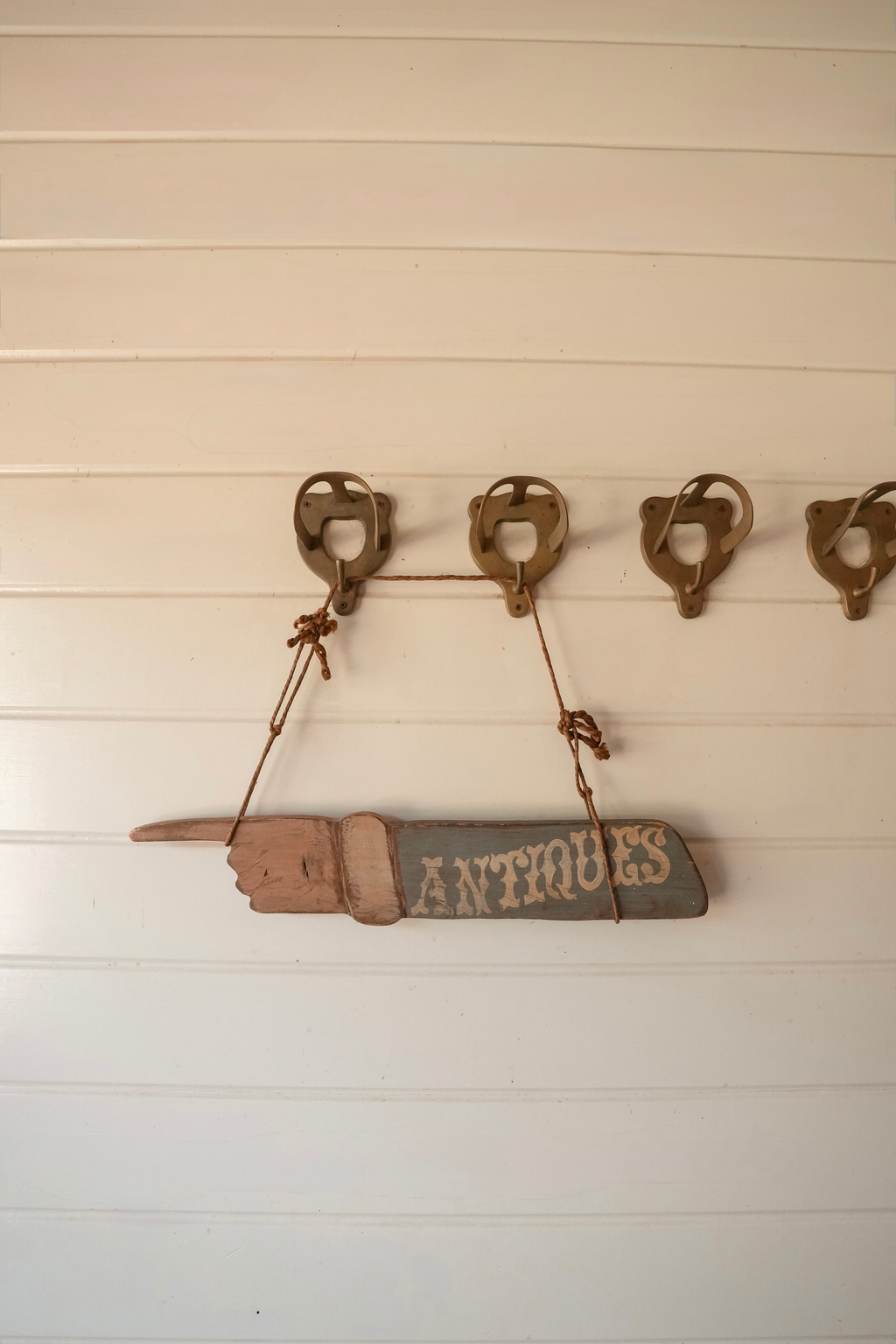 Hand-painted wooden Antiques sign shaped like a left-pointing hand, hanging from rustic rope against a wood wall.