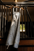 Vintage distressed herringbone utility apron with paint splatters, holes, fraying, and front pockets hanging in a horse barn. 