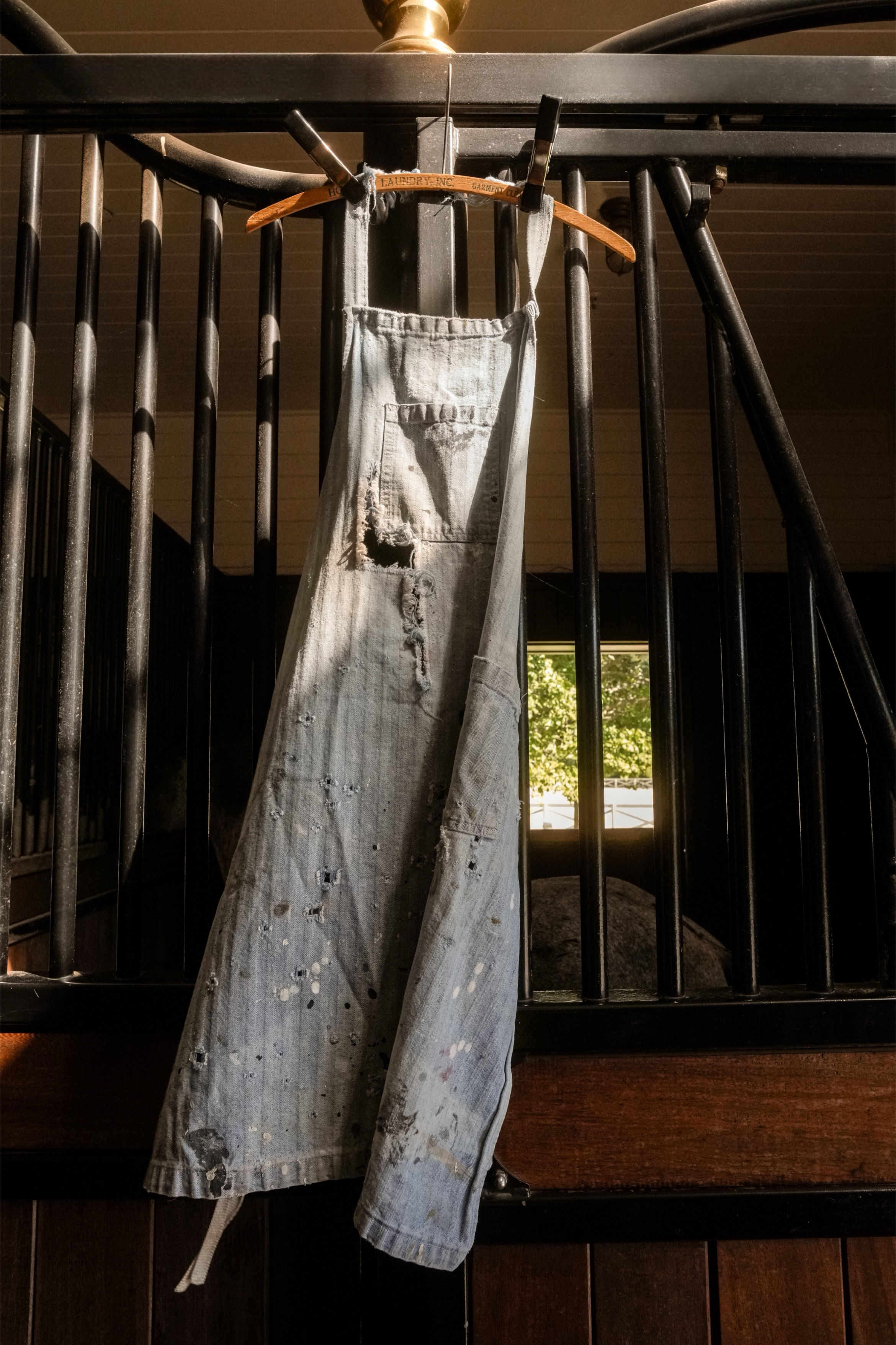 Vintage distressed herringbone utility apron with paint splatters, holes, fraying, and front pockets hanging in a horse barn. 