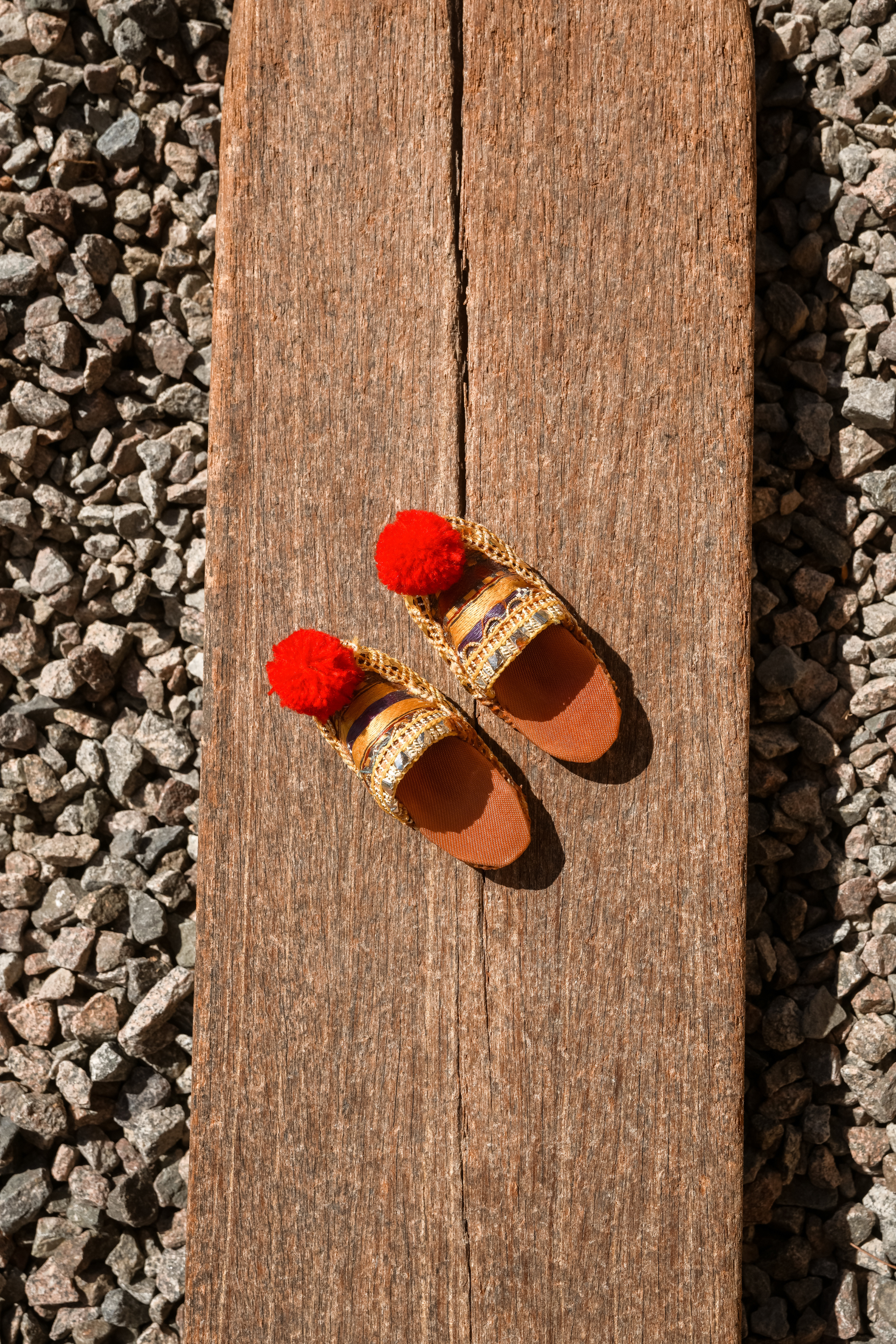 Close-up of a pair of vintage miniature Greek Tsarouchi style folk shoes with gold embroidery and red pom-poms from Alex Elle Archives