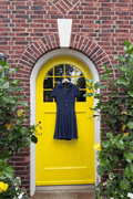Polo Ralph Lauren navy silk georgette polka dot shirt dress with short sleeves and pleated skirt in front of a yellow door. 