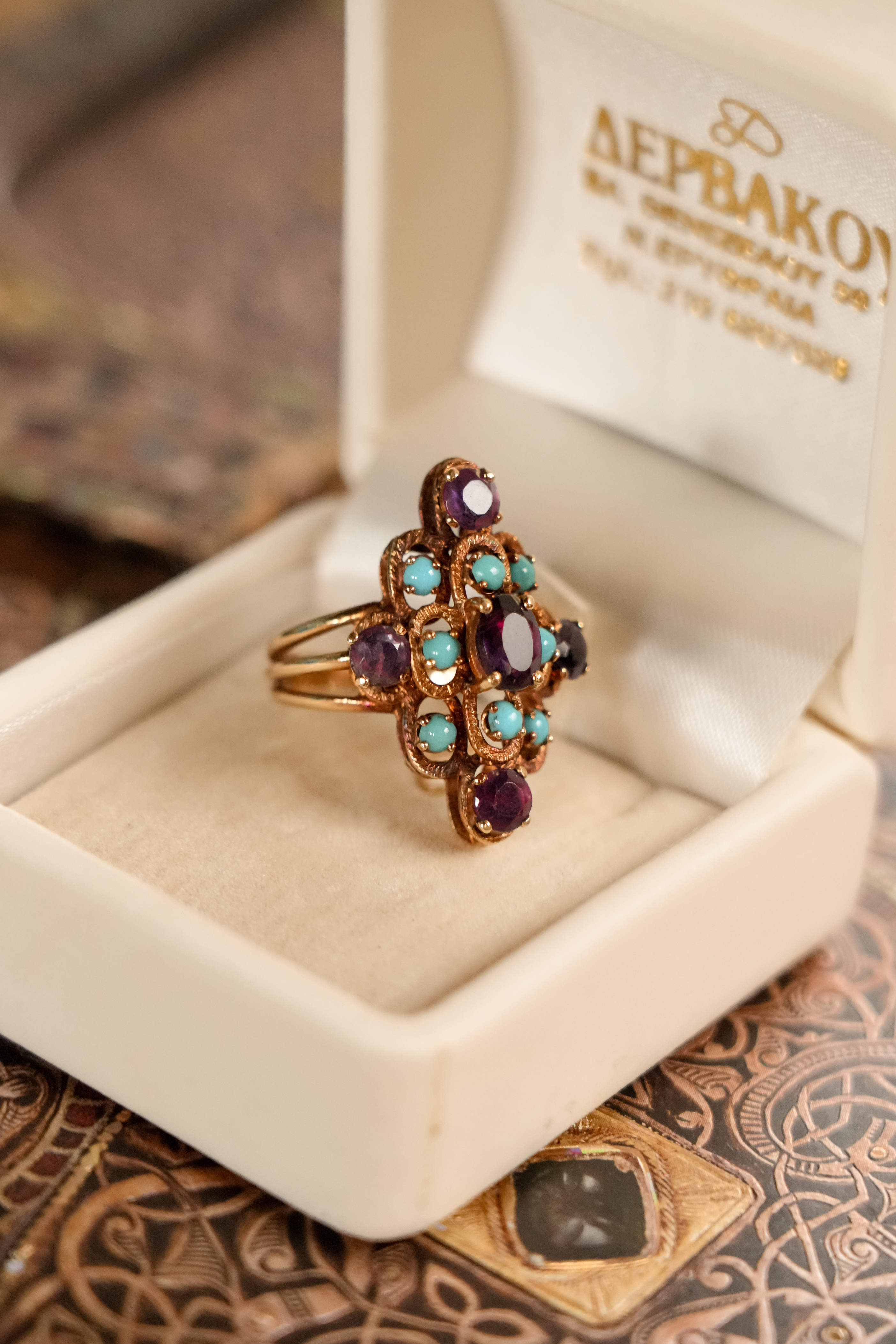 Close-up of a vintage 18k yellow gold statement ring. Displays a rich cluster of faceted purple amethysts and smooth, round turquoise cabochons set in ornate gold.