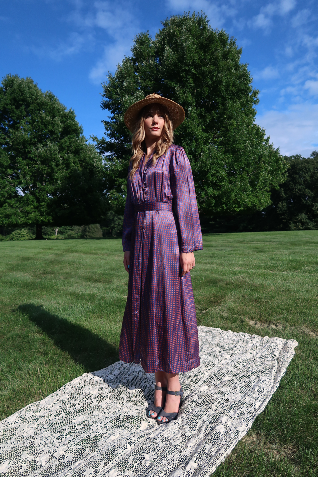 A full-length view of a woman standing outdoors on a white lace blanket wearing an authentic vintage 1970s Italian shirtwaist midi dress.