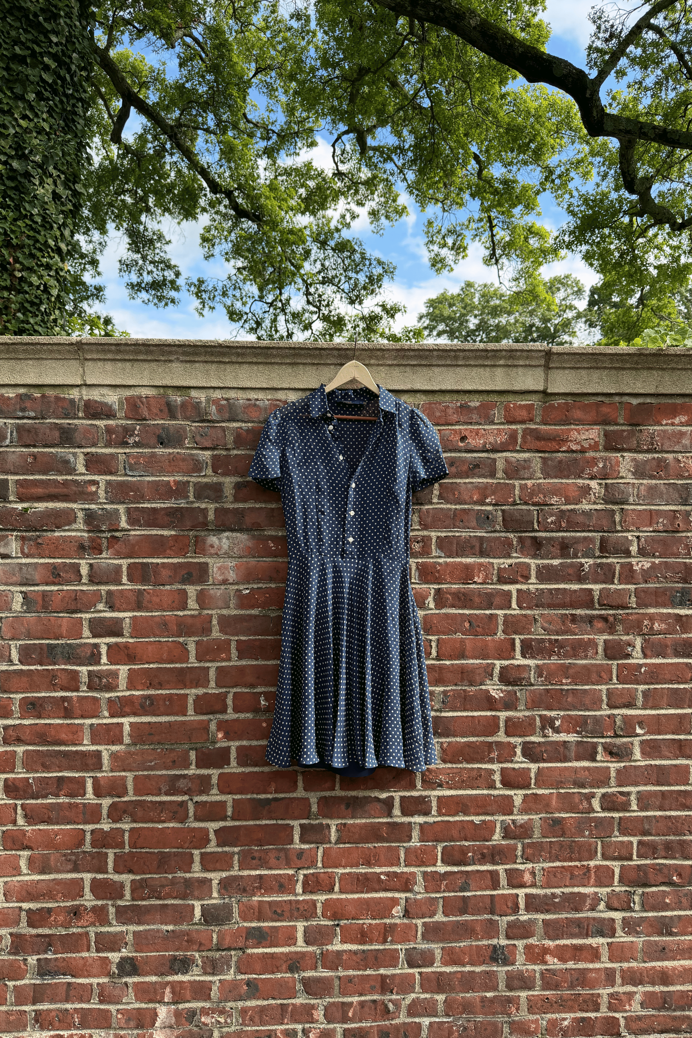 Ralph Lauren short-sleeve button-front dress hanging from a wooden hanger on a brick wall. 