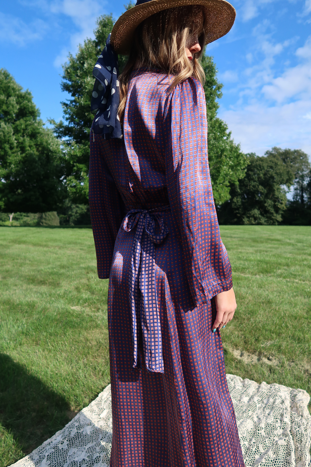 a fluid silk dress with a blue and red geometric micro pattern, featuring long bishop sleeves, a button-up front, and a matching fabric belt tied at the waist. 
