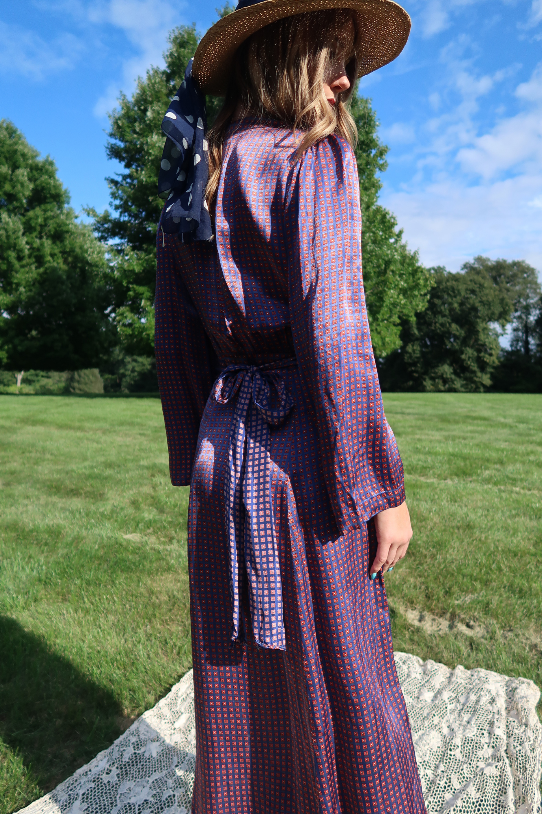 a fluid silk dress with a blue and red geometric micro pattern, featuring long bishop sleeves, a button-up front, and a matching fabric belt tied at the waist. 